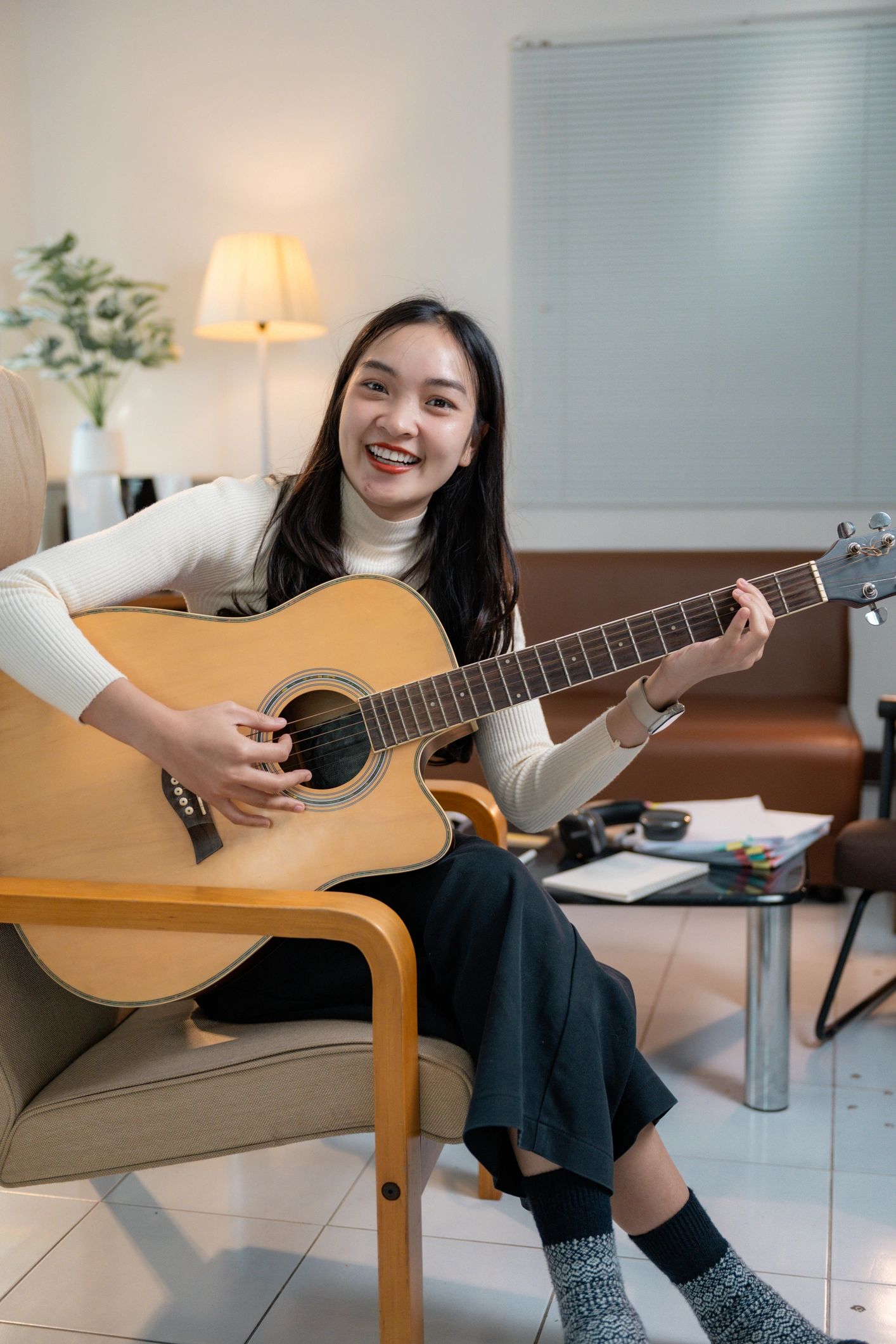 Young Asian woman sitting on chair and playing acoustic guitar