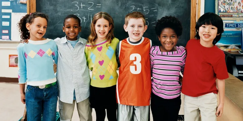 Six children smiling in a classroom in front of a chalkboard