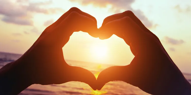Two hands forming a heart around a bright sunrise